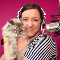 smiling Marcy Sutton holding a cat and standing next to a microphone